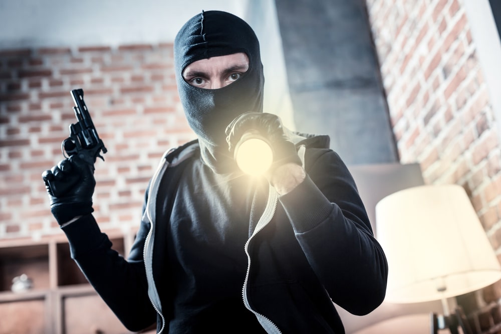 Armed masked intruder holding a gun and flashlight during a home invasion