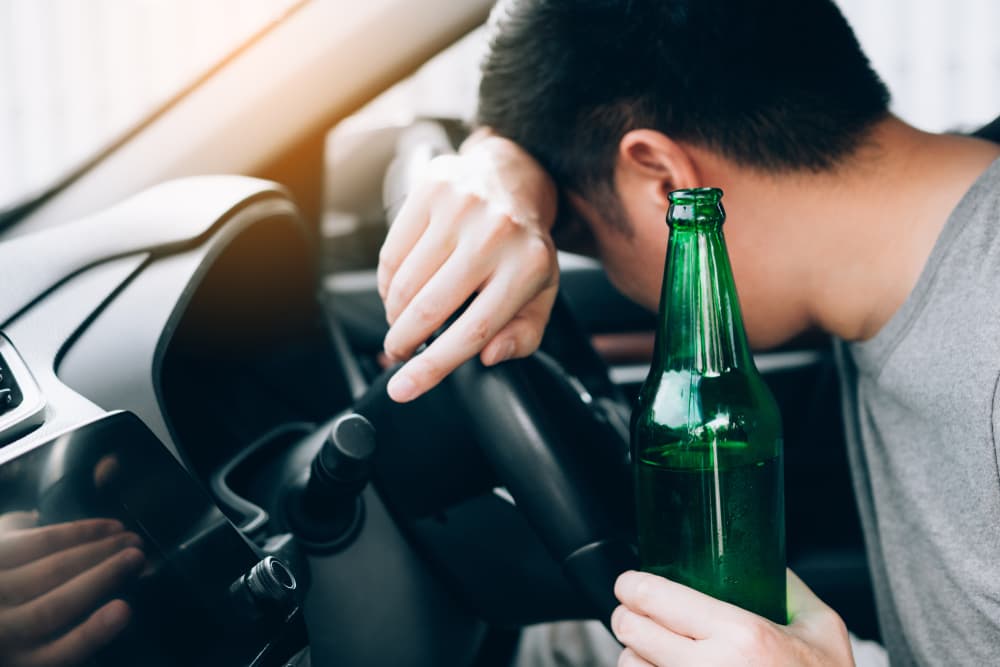 An Asian man drinks heavily until he becomes unconscious and decides to sleep at the steering wheel instead of driving home.