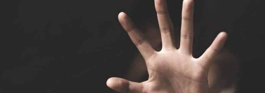A raised hand in a defensive gesture against a dark background, symbolizing fear or protection.
