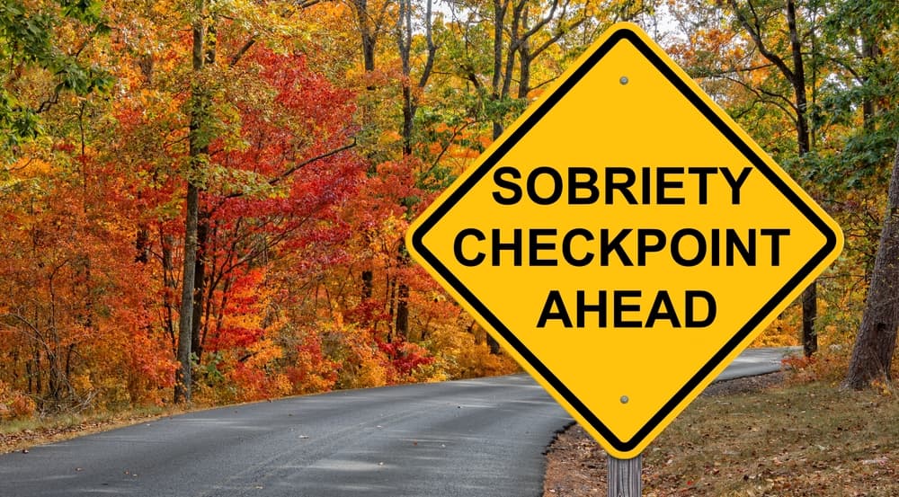 A caution sign set against a backdrop of vibrant autumn foliage, reminding drivers to remain sober and cautious on the road.