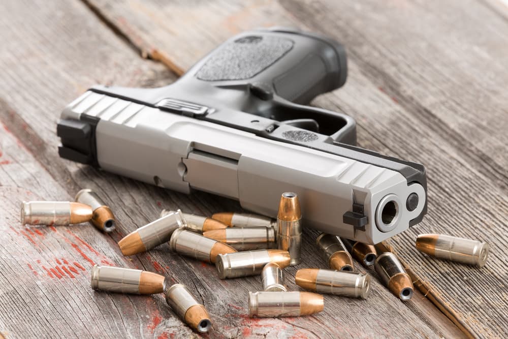 Close-up of handgun barrel amid scattered bullets on rustic wood, symbolizing crime.