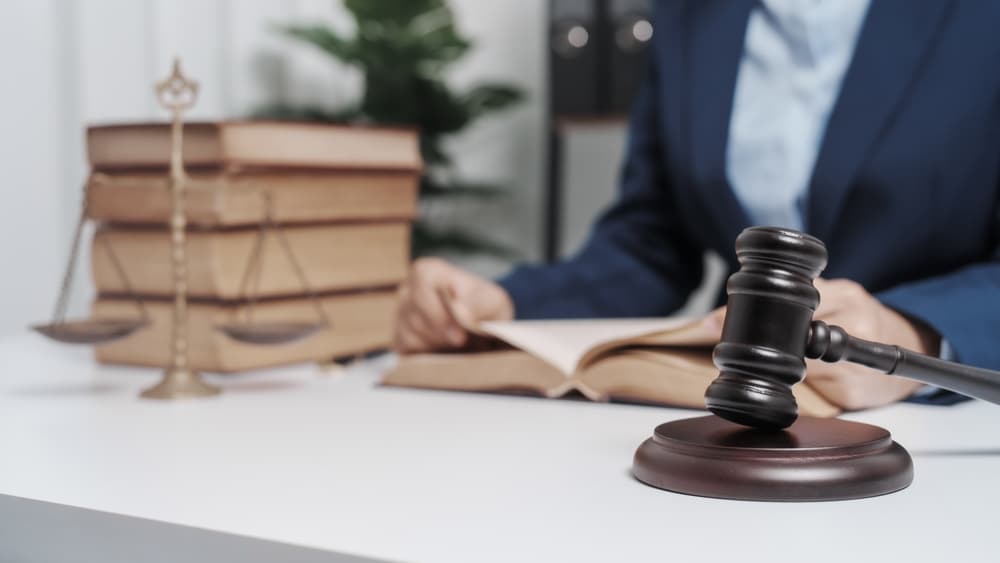 A young female lawyer in a formal suit, working on real estate law. She's surrounded by law books and contract documents, preparing arguments for a defense strategy.






