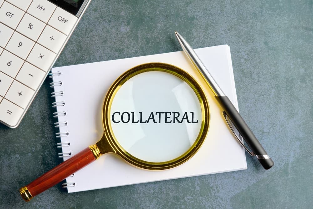 A composition showing the word "COLLATERAL" through a magnifying glass on a notebook, with a calculator and pen in the background.