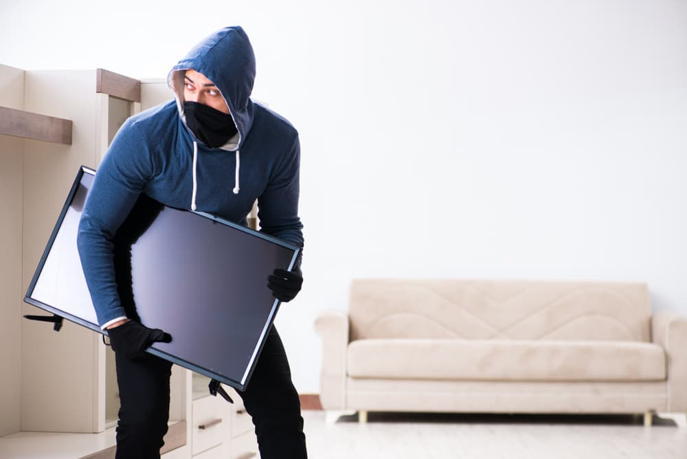 A man breaking into a house and stealing a television set.