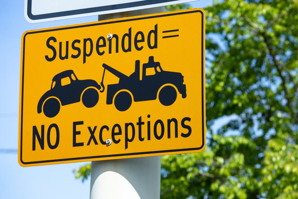 Road signs reading "Suspended License = Towed Car. No Exception" along a roadway, with blank space on the right for additional text.