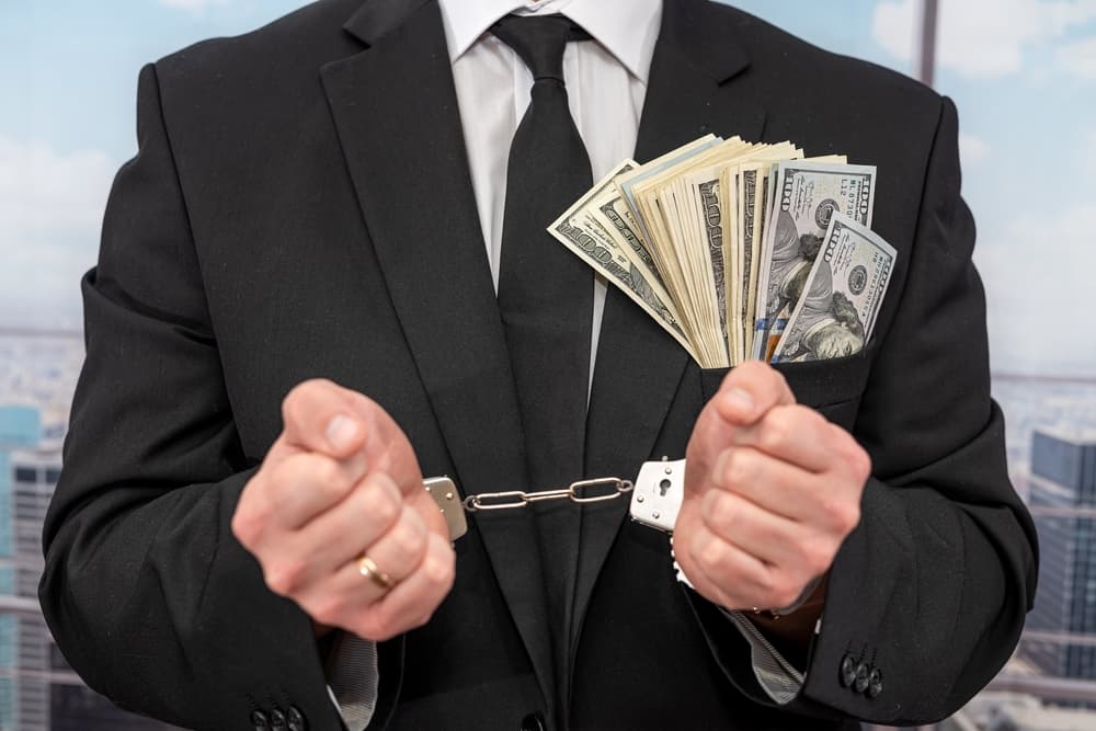 A businessman in a classic suit sitting at a table with his hands in handcuffs, illustrating the concept of a criminal restrained by law.