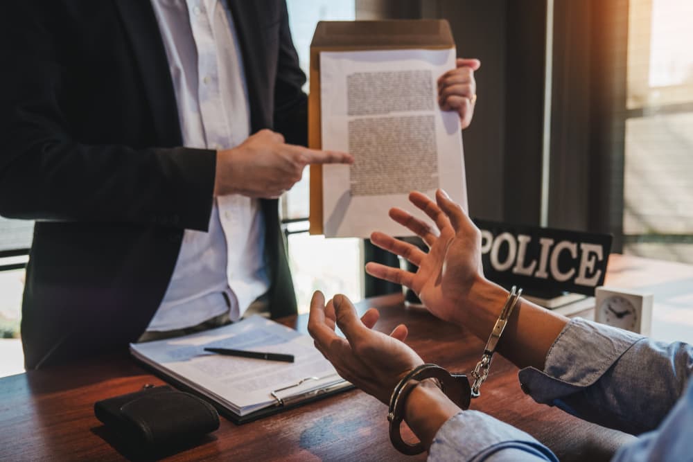 A law enforcement officer interrogates a male suspect in handcuffs inside an investigation room, conducting an interview regarding the alleged crime.