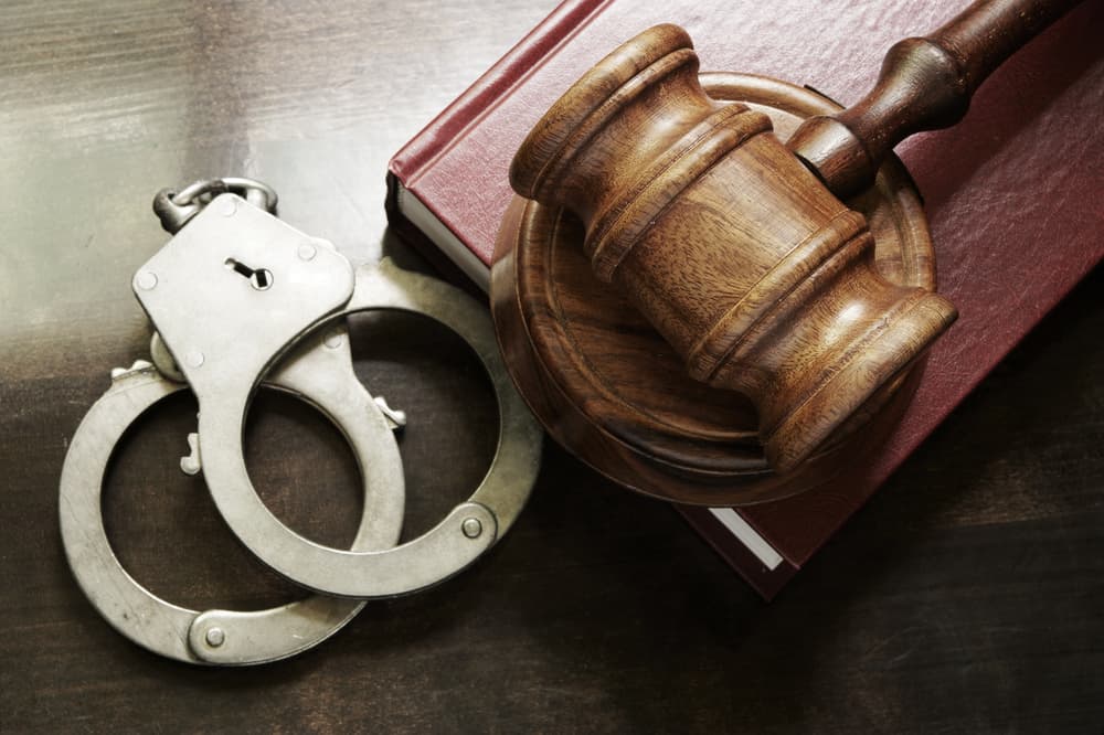 A judge's gavel, handcuffs, and a red legal book placed on a wooden table.