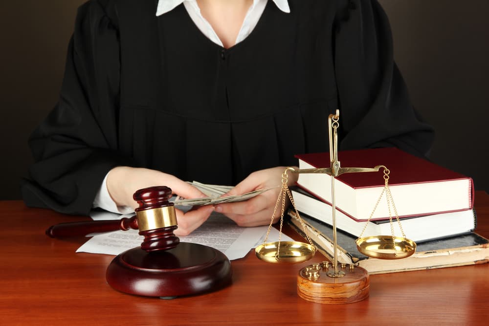 A judge sitting at a table during court hearings, with a black background.






