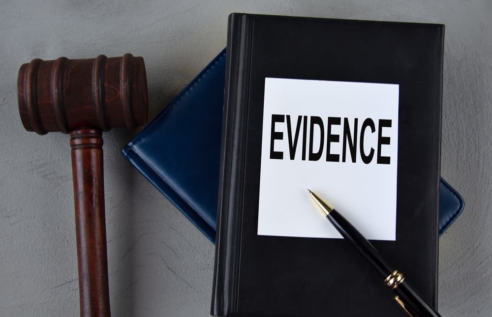 The word "EVIDENCE" displayed on a white sheet, accompanied by leather notebooks, a judge's gavel, and a pen.