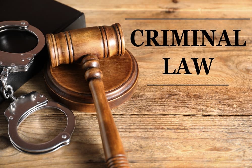 A book, judge's gavel, and handcuffs on a wooden table symbolizing criminal law and justice.