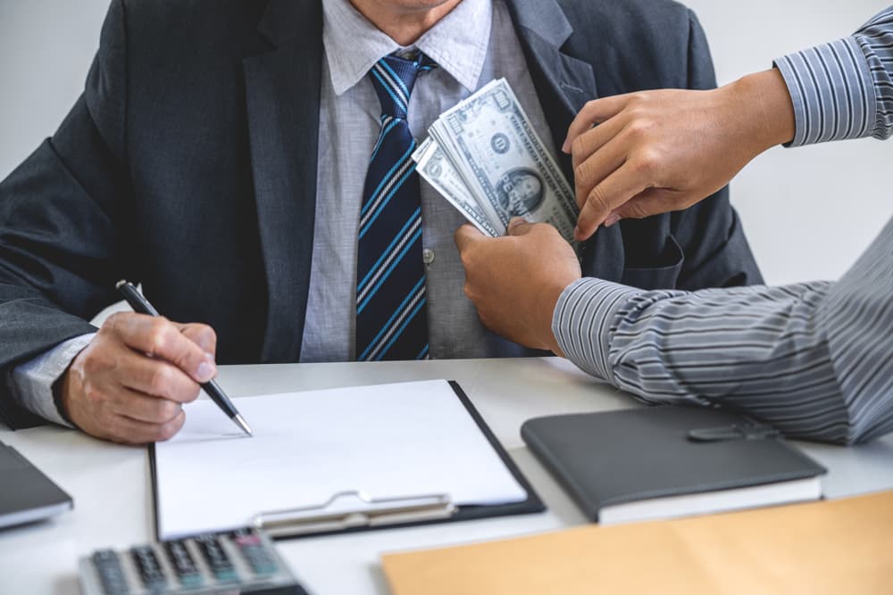 Bribery and corruption concept: Consultant receiving dollar bills from a businessman in exchange for a real estate corporate contract and financial deal agreement.







