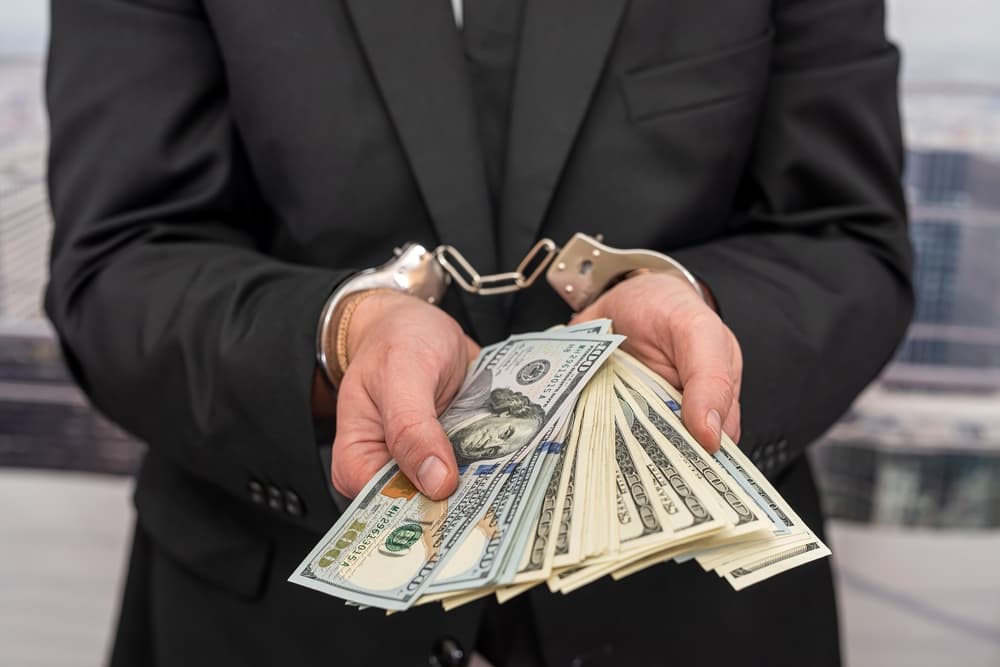 Young male businessman in a classic suit and tie, hands cuffed, representing the concept of a man in handcuffs.