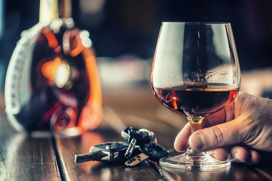 Person holding a glass of alcohol with car keys on the table, illustrating the importance of choosing a lawyer with local Los Angeles DUI experience.